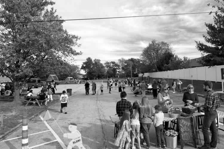 Families and kids gathered at an outdoor fall festival with a bounce house and hay bales